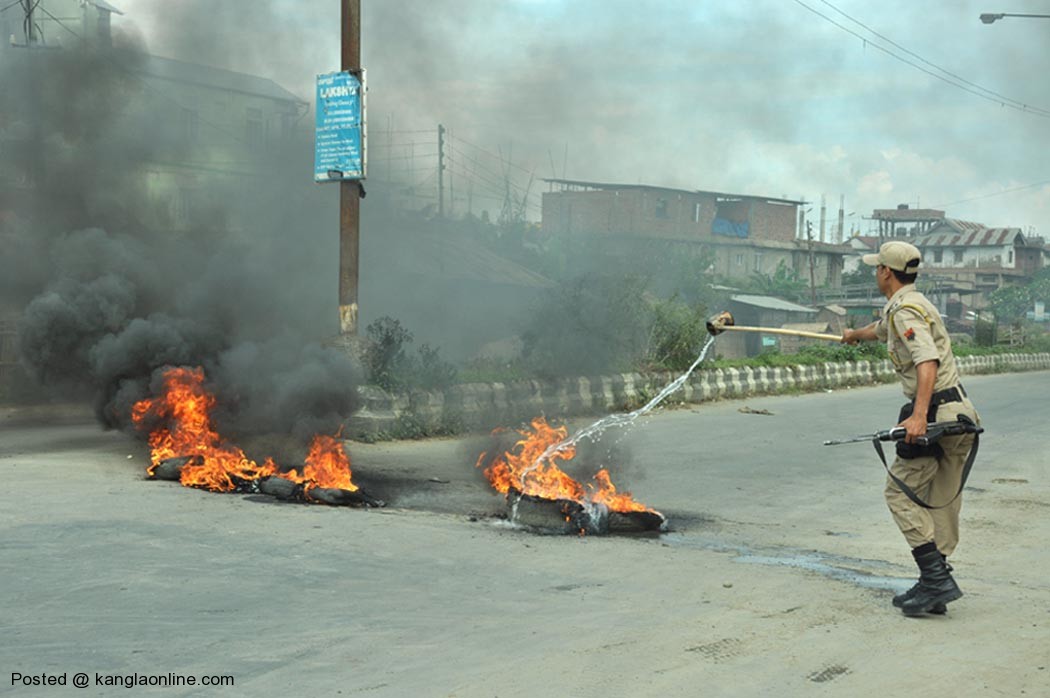A police personnel tries to douse tyres burning along the Uripok road set ablaze by bandh supporters on Thursday.